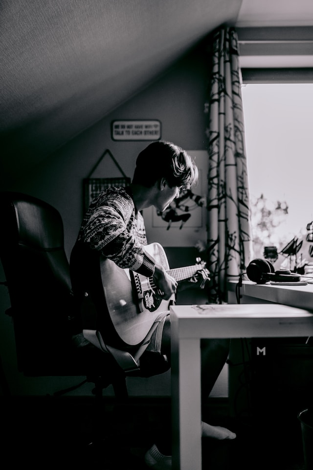 black and white photo of man playing guitar in a room